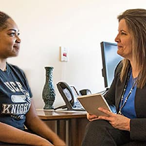Two women sit facing each other with slight smiles on their faces during a counseling session.