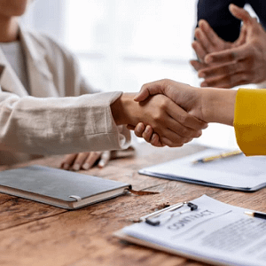 Hands shaking in agreement above signed contract at a table