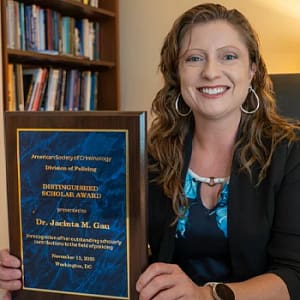 Jacinta Gau sits at her desk, holding her plaque from the American Society of Criminology’s Division of Policing.
